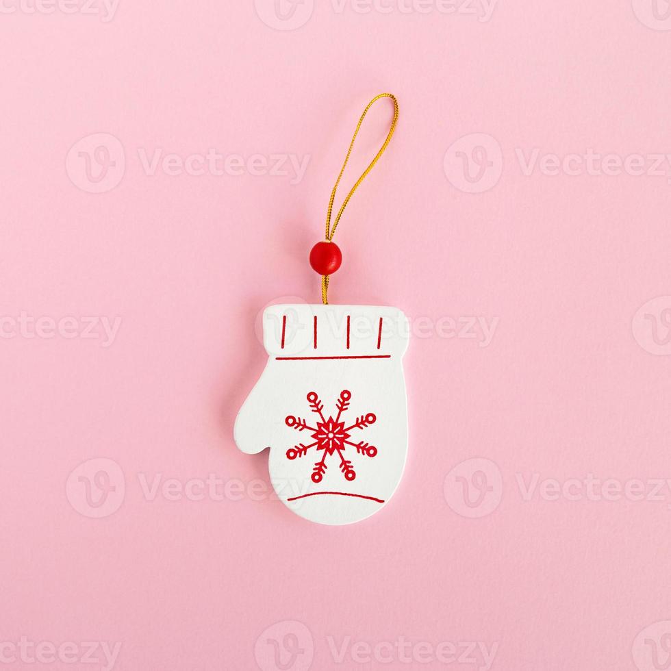 Wooden Christmas and New Year decoration in the form of mitten with painted red snowflake on a pink background, top view. photo