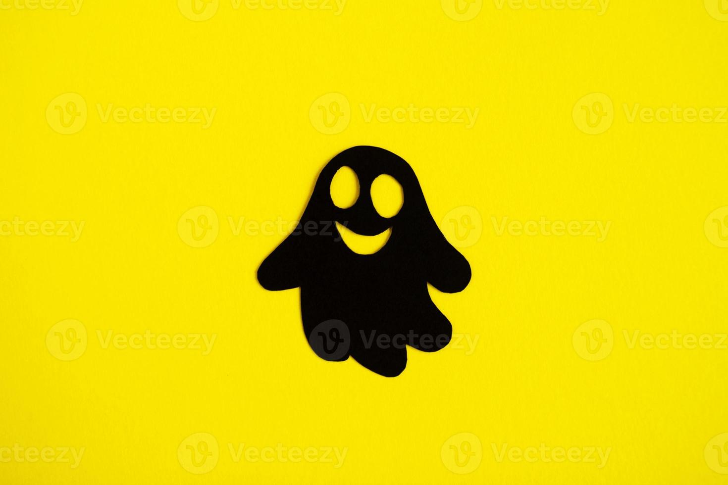 Holiday decorations for Halloween. Black paper ghost on a yellow background, top view. photo