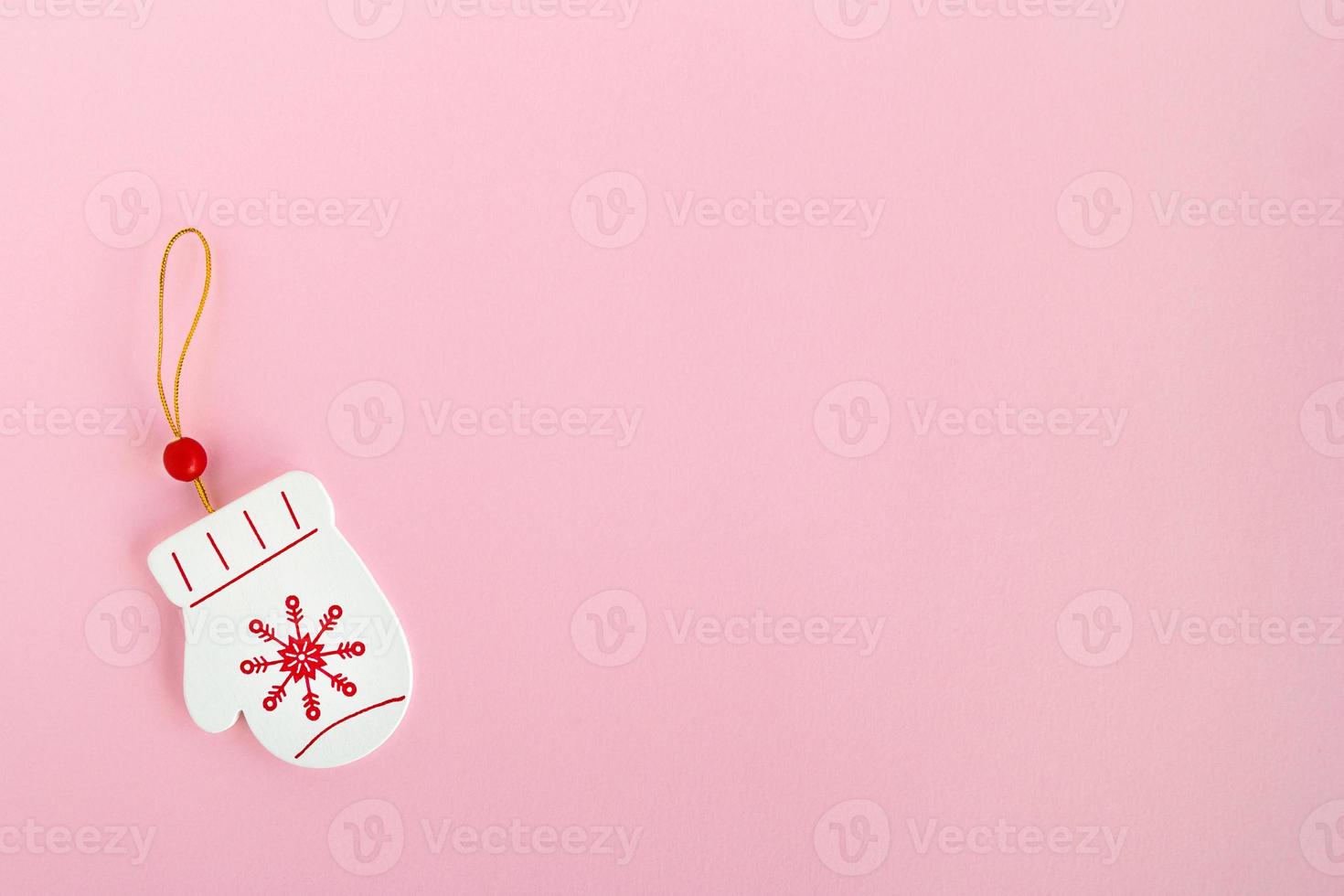 Wooden Christmas and New Year decoration in the form of mitten with painted red snowflake on a pink background, top view. photo