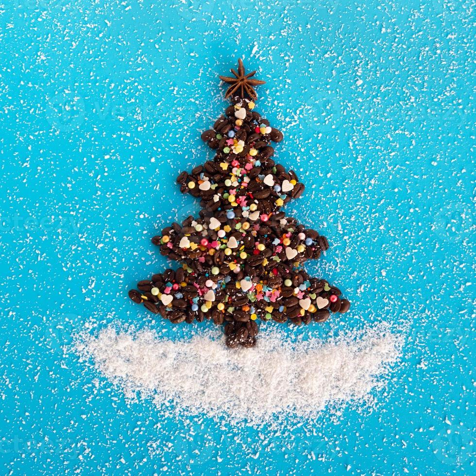 árbol de navidad hecho de granos de café y estrella de anís decorada, aspersión culinaria multicolor y chips de coco sobre un fondo azul, vista superior. foto