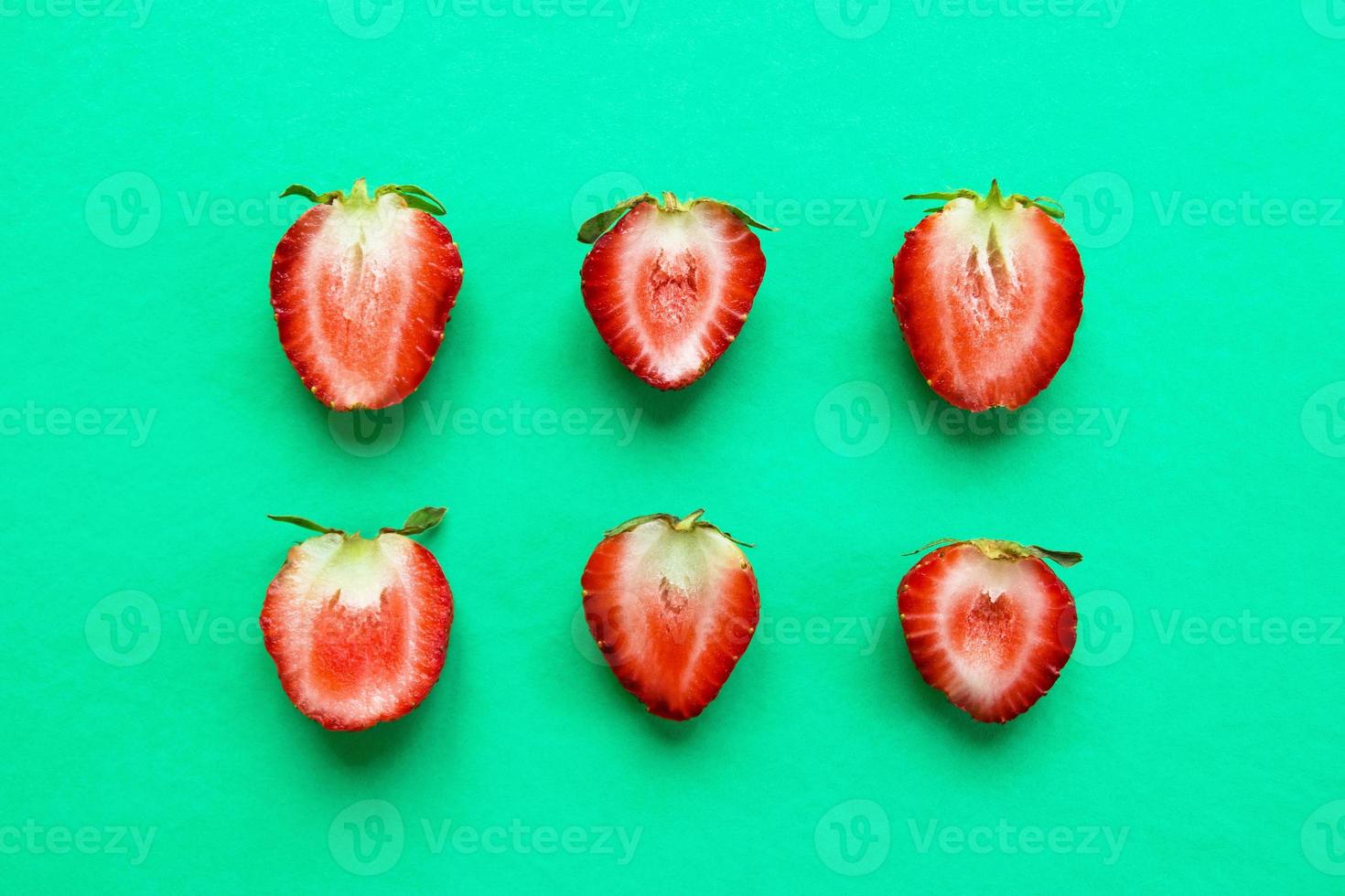 Two rows from halves of red ripe strawberry on a bright turquoise background, top view. Healthy summer food. photo