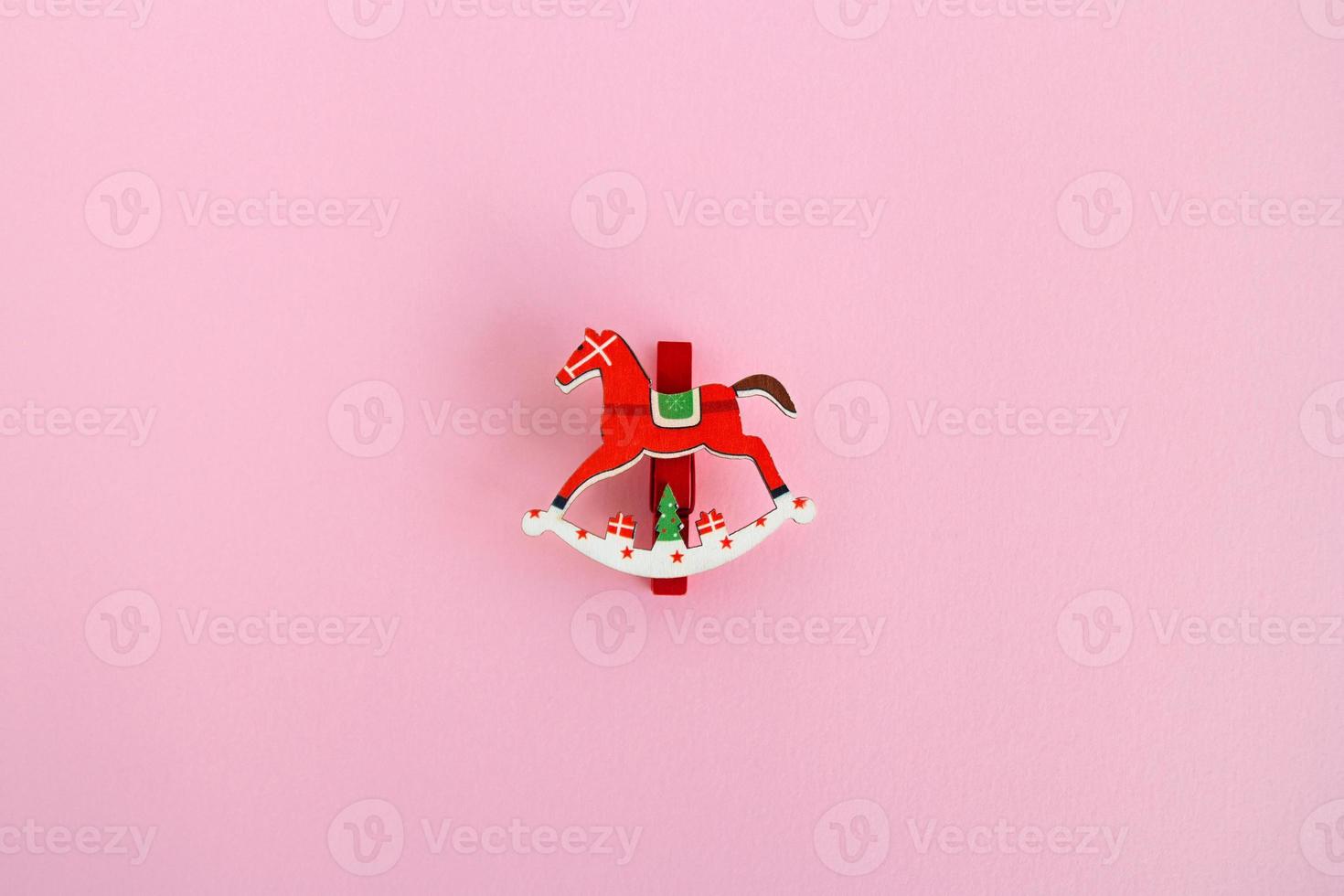 Red wooden Christmas and New Year decoration in the form of horse on a pink background, top view. photo