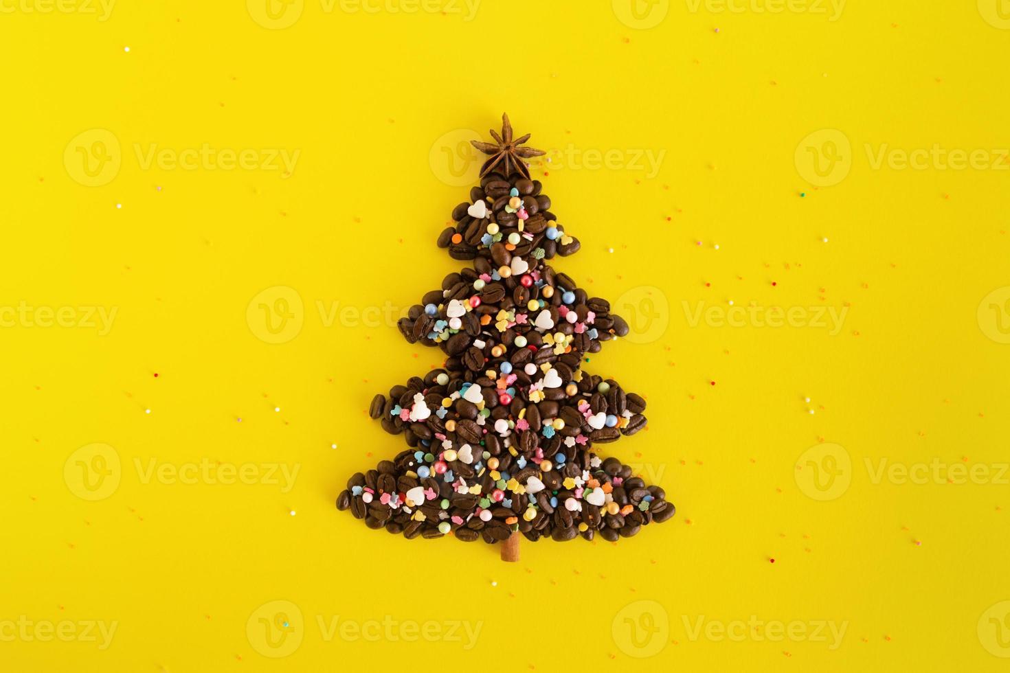 Winter composition with Christmas tree made by coffee beans and decorated anise star, cinnamon stick and multicolored culinary sprinkling on a yellow background, flat lay. Greeting card for New Year. photo