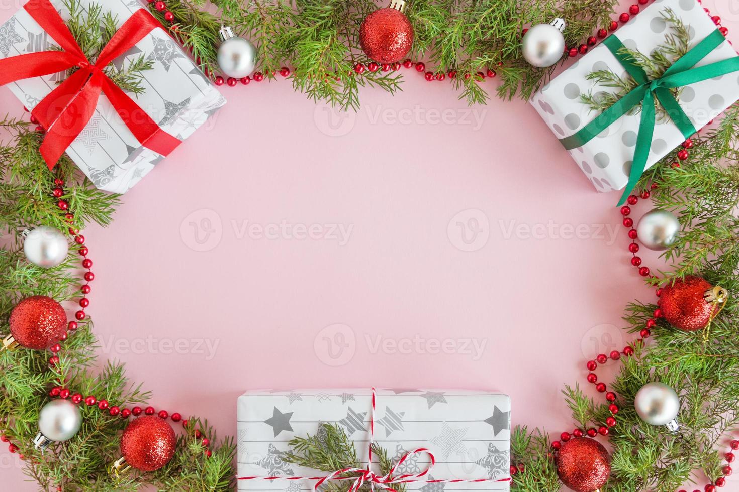 vista superior en un marco de adornos navideños rojos y plateados, cajas de regalo y ramas de abeto sobre un fondo rosa con espacio para copiar. foto