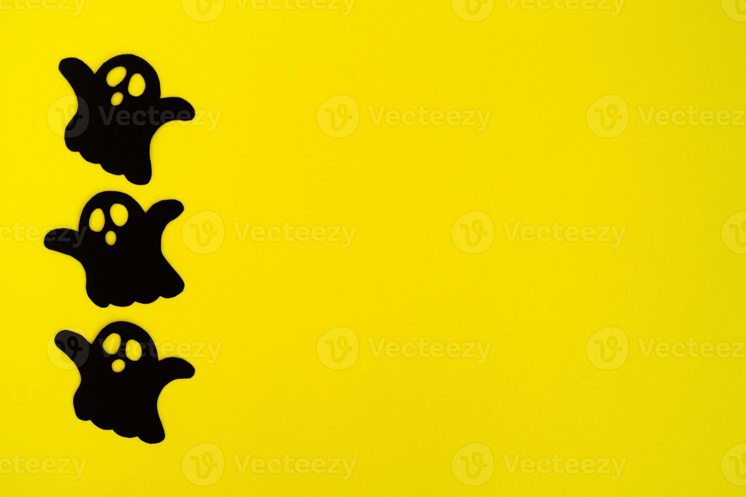 Holiday decorations for Halloween. Three black paper ghosts on a yellow background, top view. photo