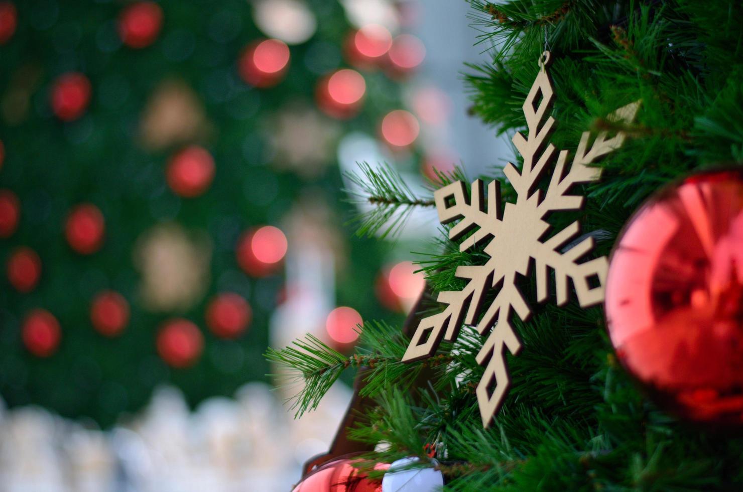Red bauble and other ornament hanging on Christmas tree with bokeh background from another Christmas tree photo
