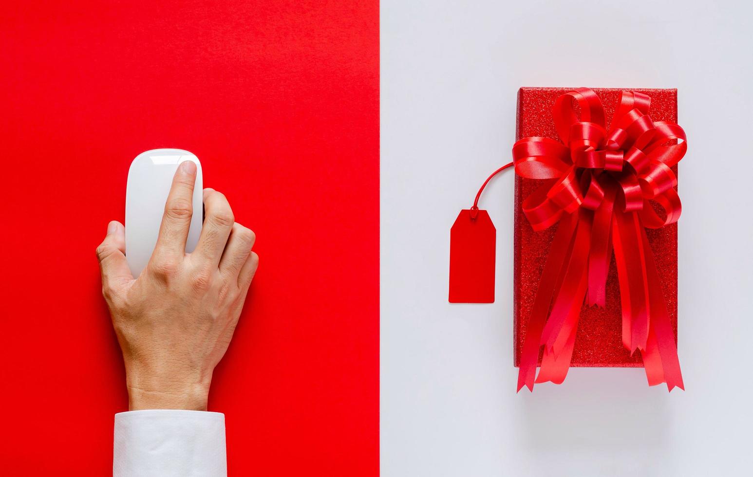 mano usando el mouse comprando en línea con caja de Navidad roja y etiqueta de precio sobre fondo blanco y rojo. concepto de lunes cibernético. foto