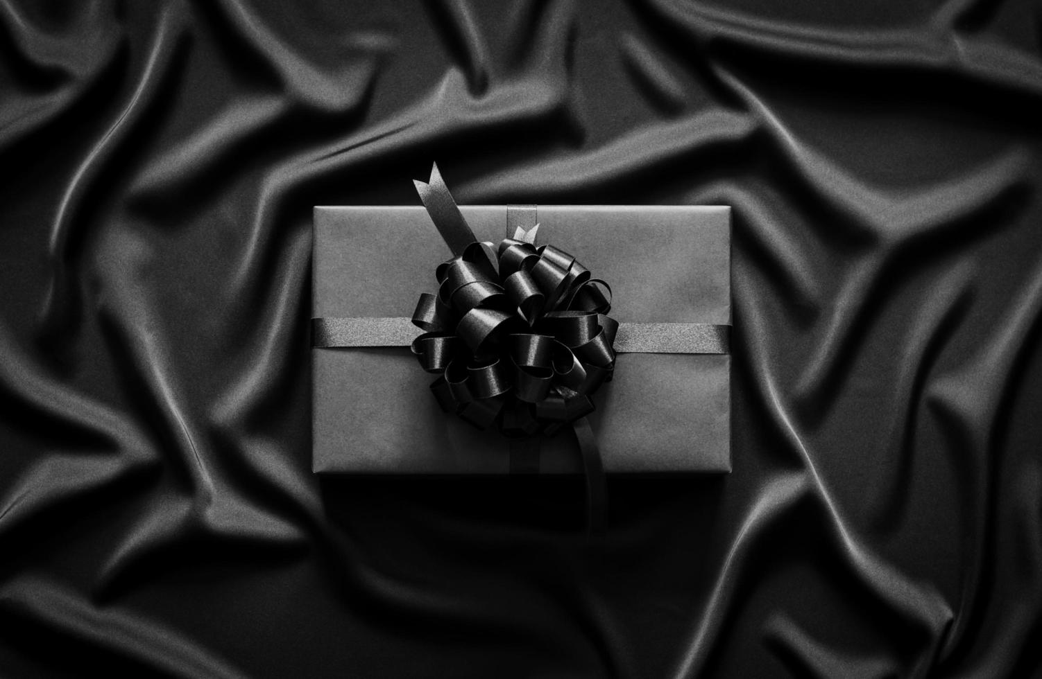 A black gift box with ribbon puts on black wavy cloth. Black friday and Boxing day concept. photo