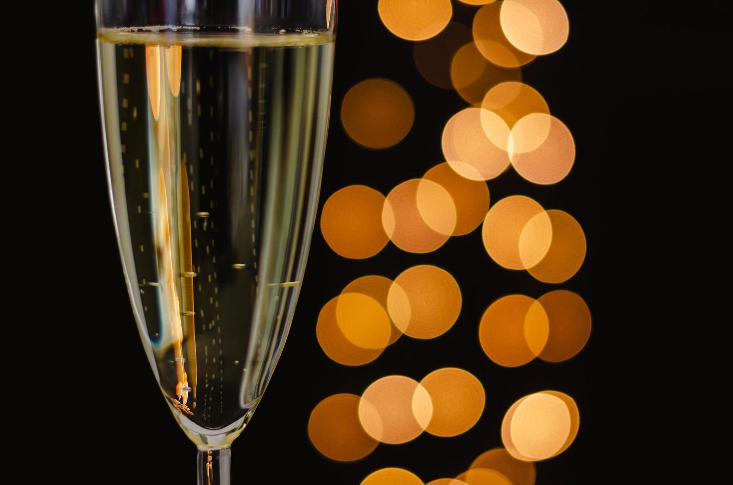 Partial focus of a glass of sparkling wine with golden bokeh lights on dark background. photo