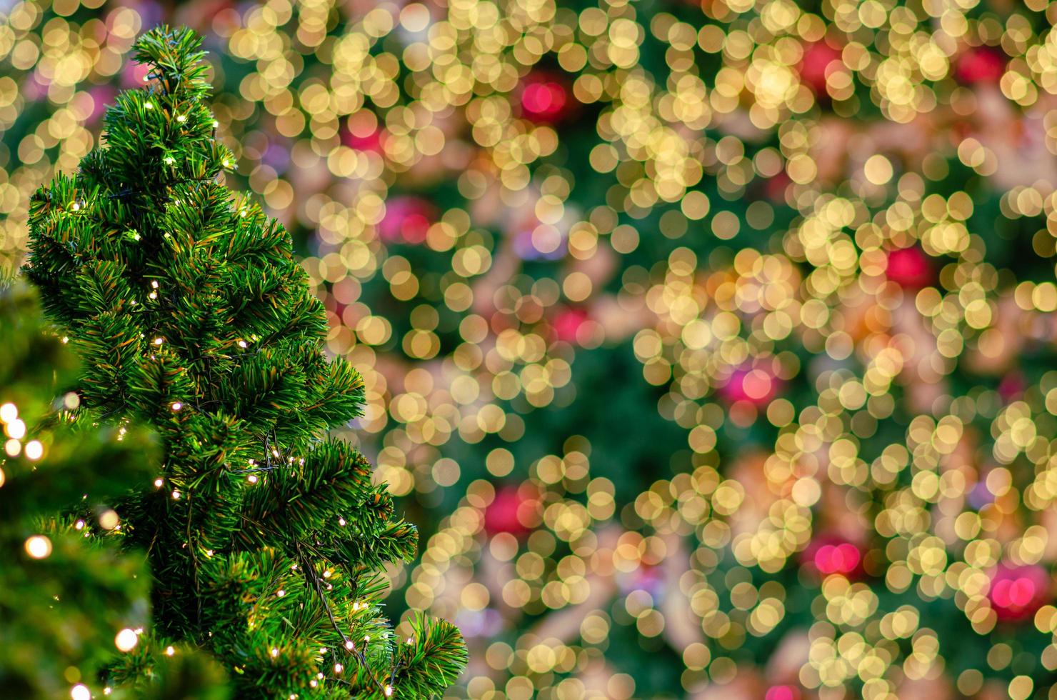 pequeño árbol de navidad con fondo de luces bokeh de otro grande para el festival navideño. foto