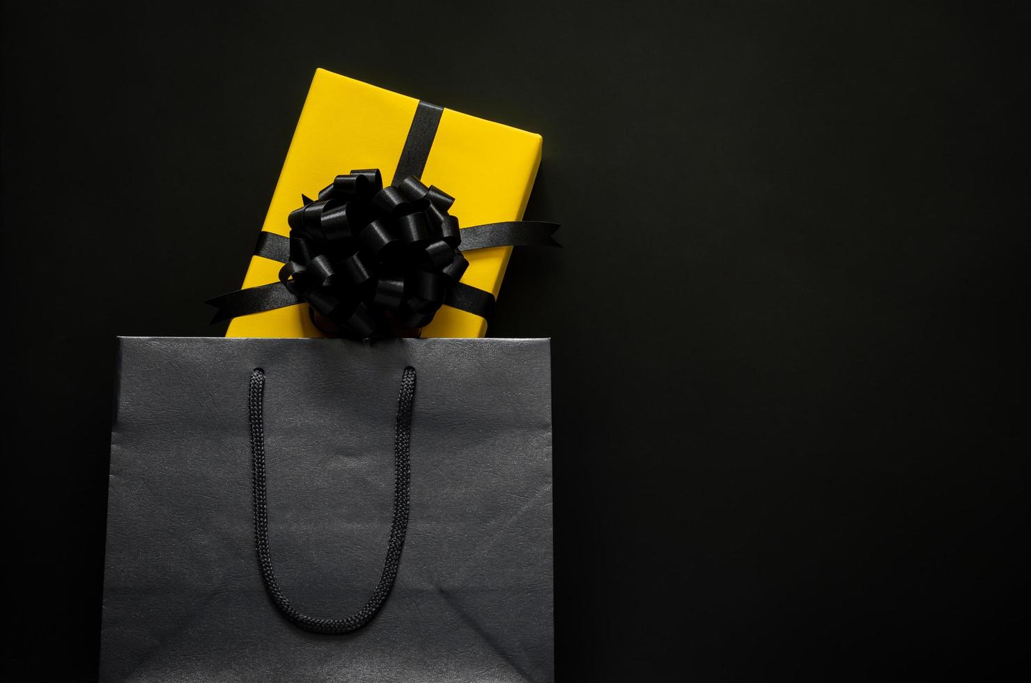 A yellow gift box puts in black shopping bag with black background. Black friday and Boxing day concept. photo