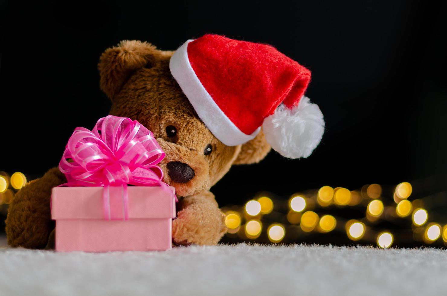 Brown teddy bear wearing santa claus hat holding blurred focus of Christmas gift box and bokeh lights background. photo