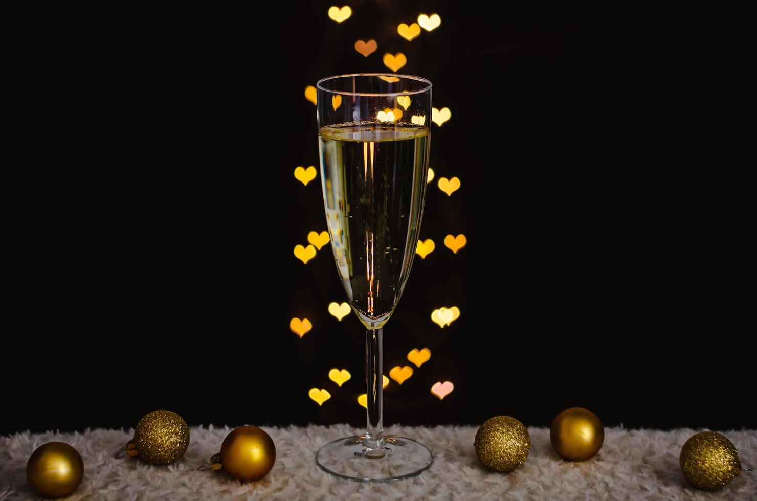 A glass of sparkling wine with golden christmas ornaments with love shape bokeh lights on dark background. photo