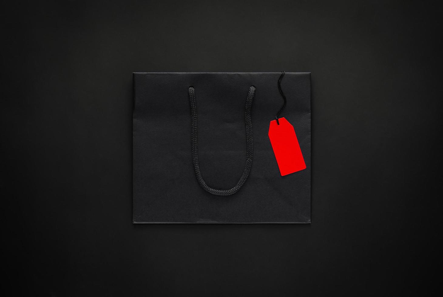 Black shopping paper bag with blank red price tag on black background for Black Friday shopping sale concept. photo