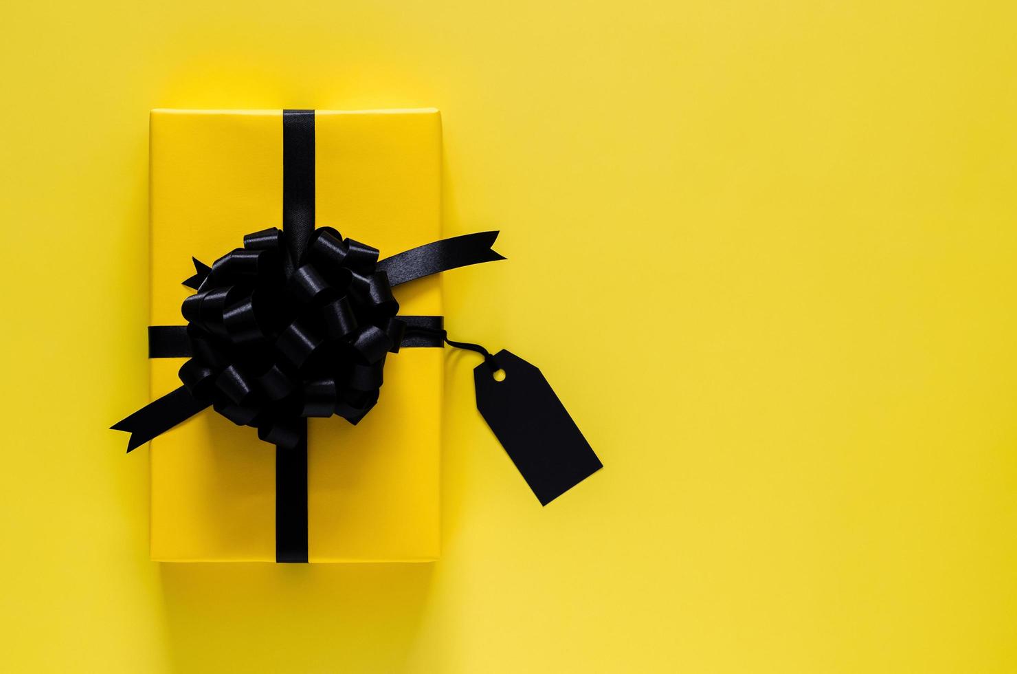 A yellow gift box with black ribbon and blank price tag puts on yellow background. Black friday and Boxing day concept. photo
