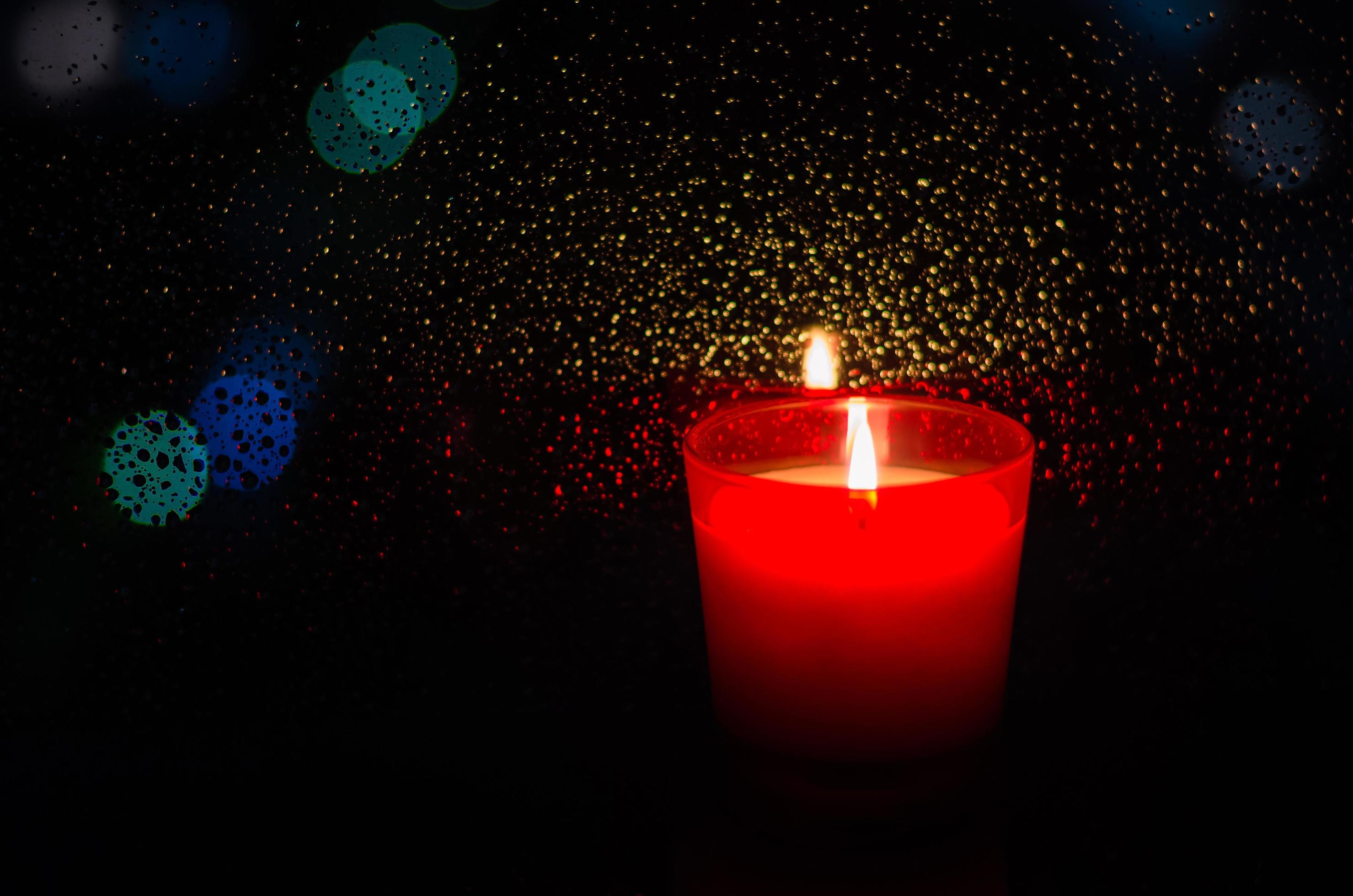 Burning candle in red glass puts beside window with rain drop on bokeh