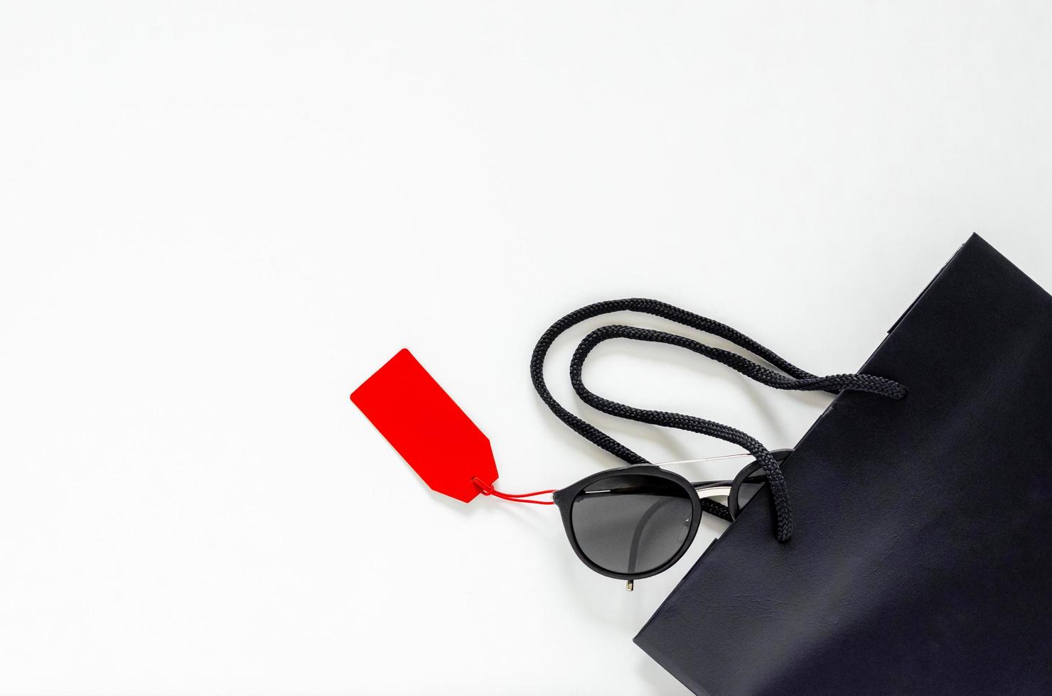 Flat lay of black sunglasses with red price tags and shopping bag on white background for Black Friday sale concept. photo