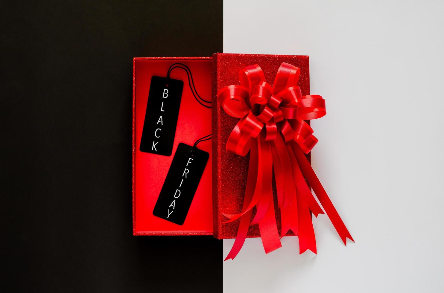 Red christmas box with red bow ribbon and black price tag on black and white background. Black Friday concept. photo