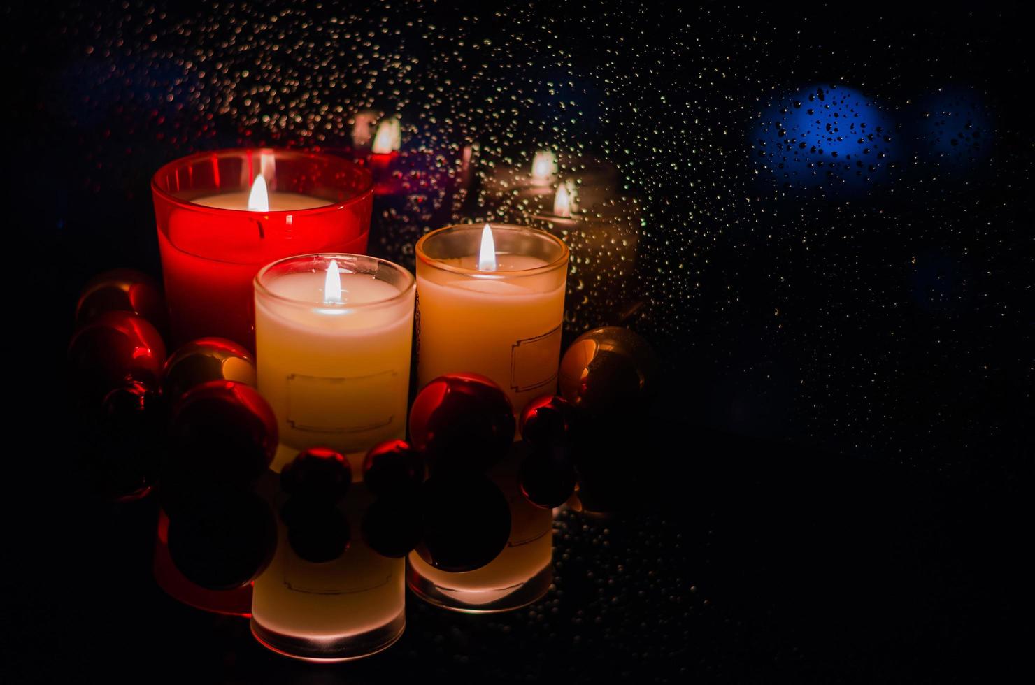 Focus and blurred of burning candles with Chirstmas ornaments put beside window that have rain drop in dark background. photo