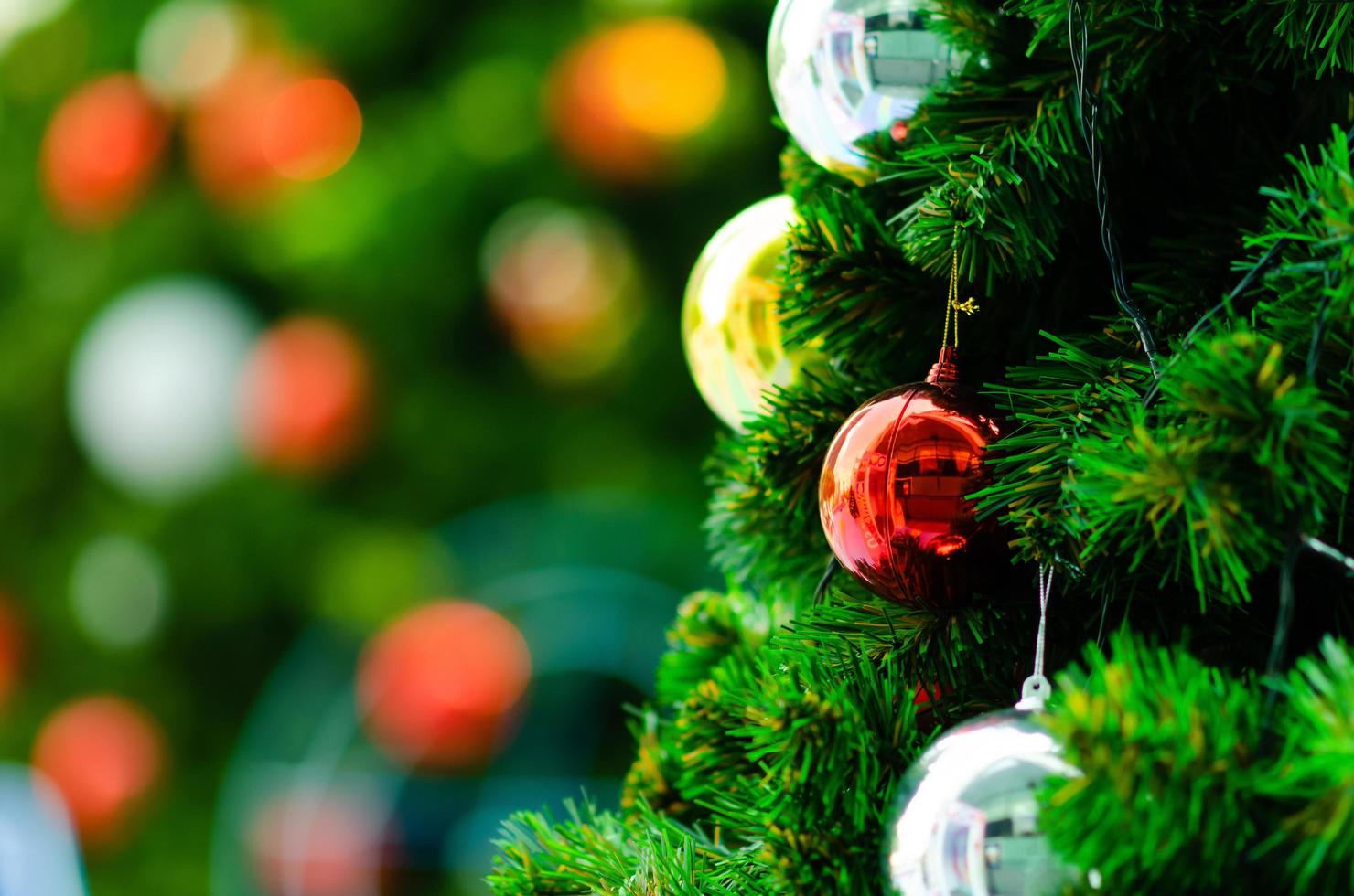 Red bauble and other ornament hanging on Christmas tree with bokeh background from another bigger Christmas tree. photo