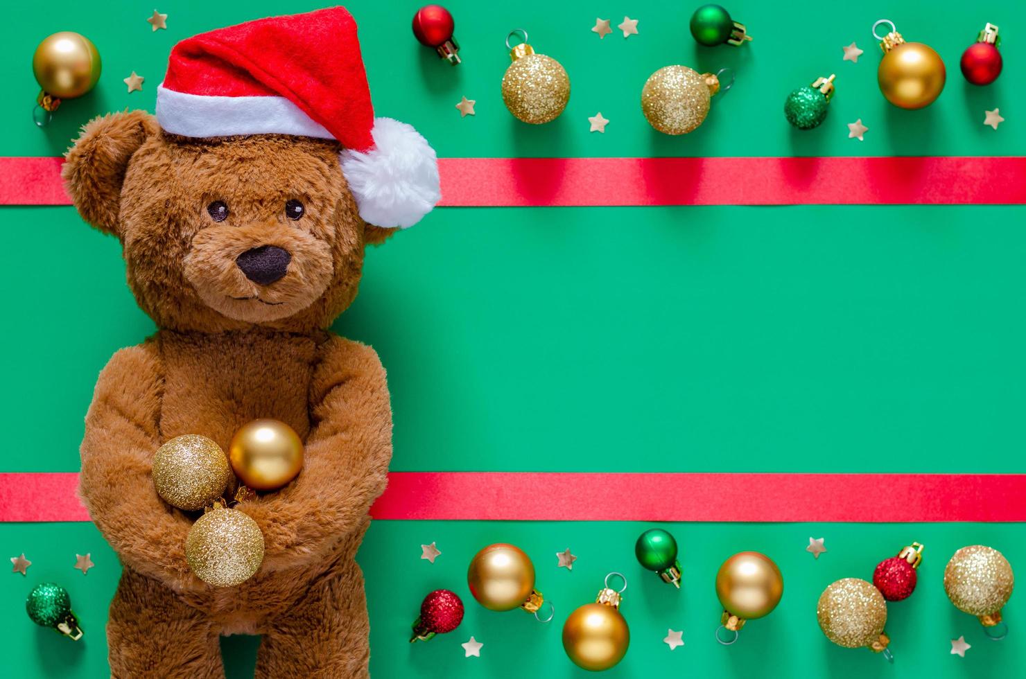 Smiling teddy bear holding Christmas baubles on blurred green background with ornaments. Christmas and New year concept. photo