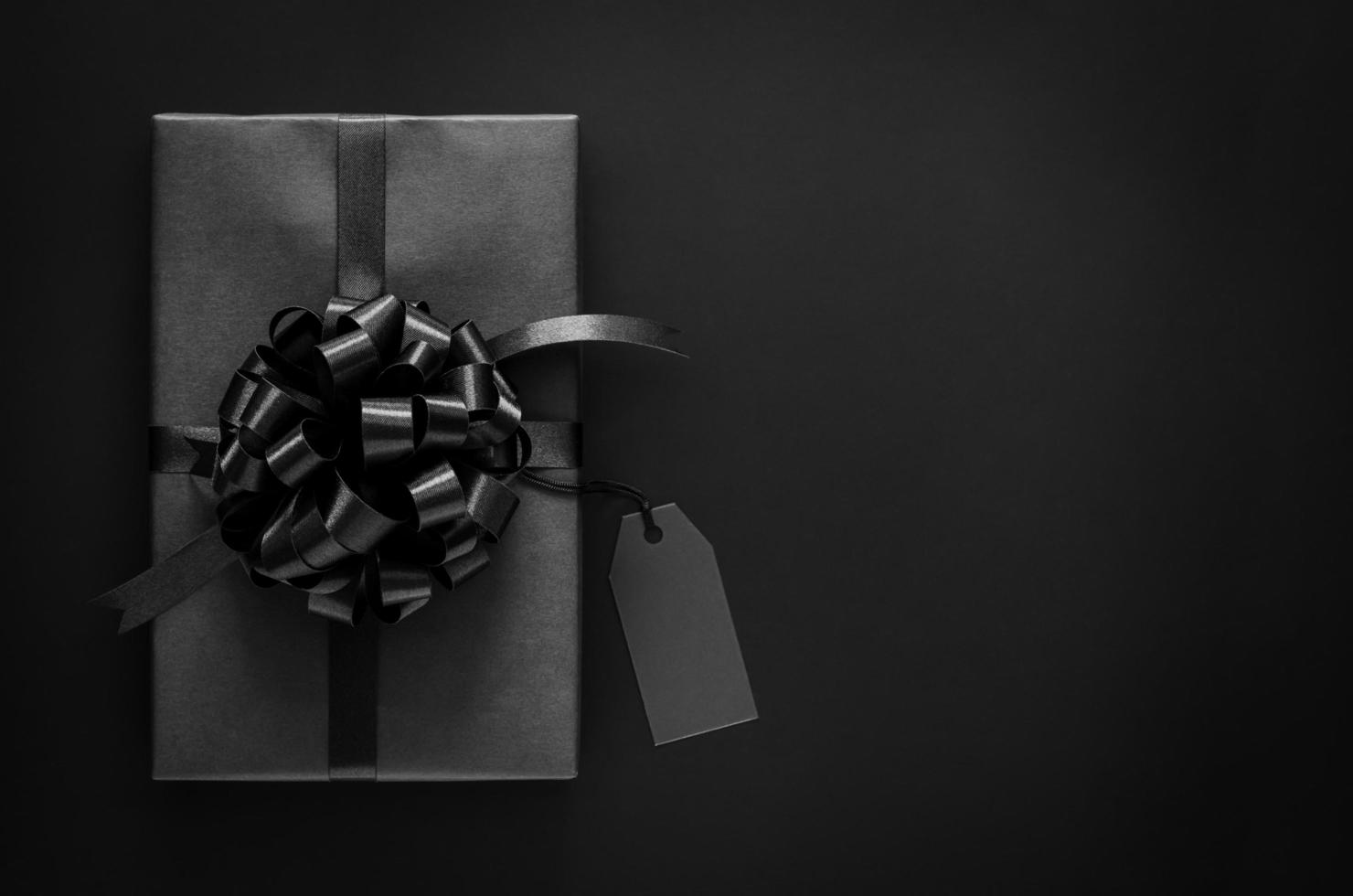 A black gift box with ribbon and blank price tag puts on black background. Black friday and Boxing day concept. photo