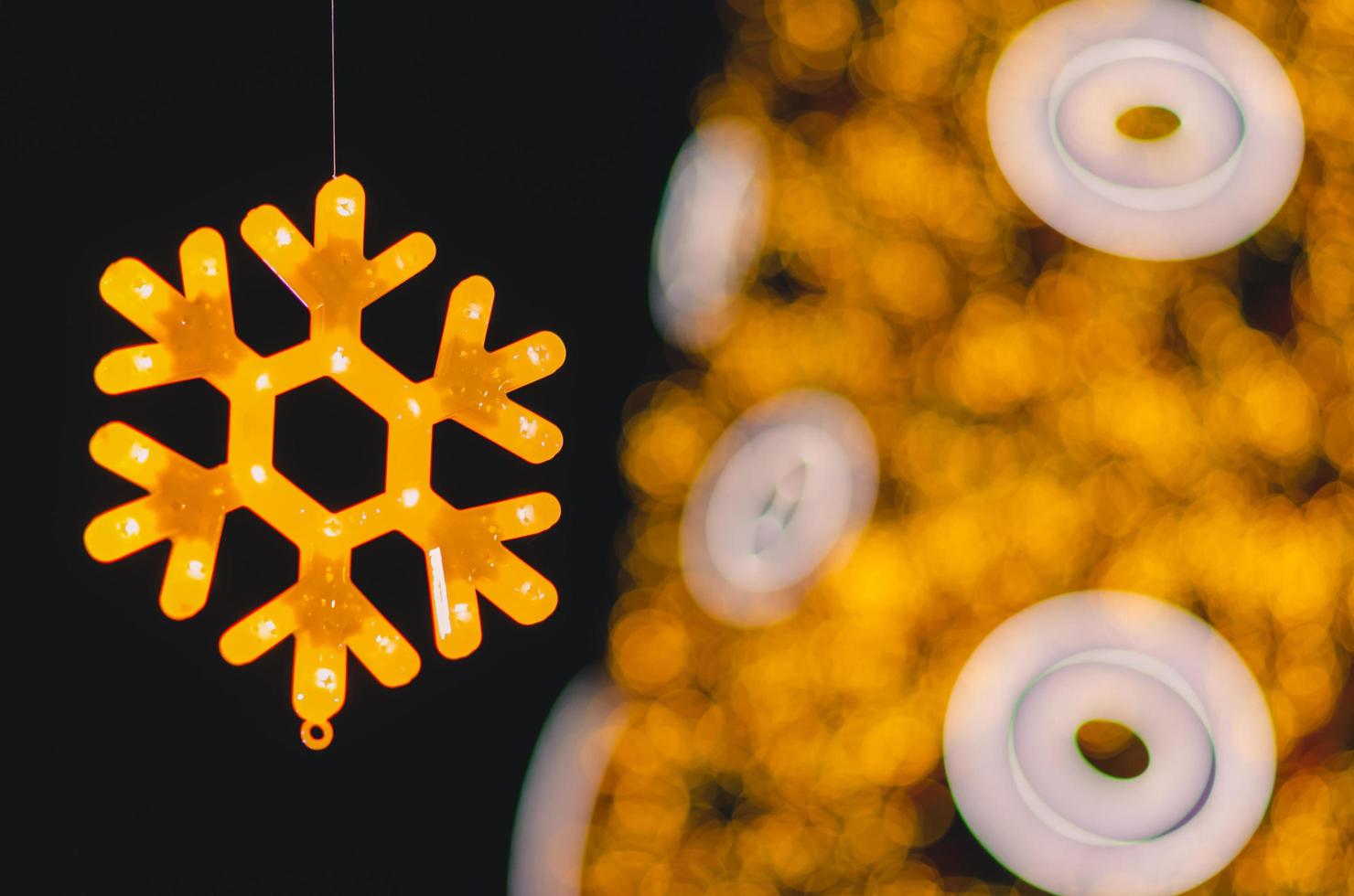 Partial focus of neon lights snow flake Christmas ornament with blurry Chirstmas tree background. photo