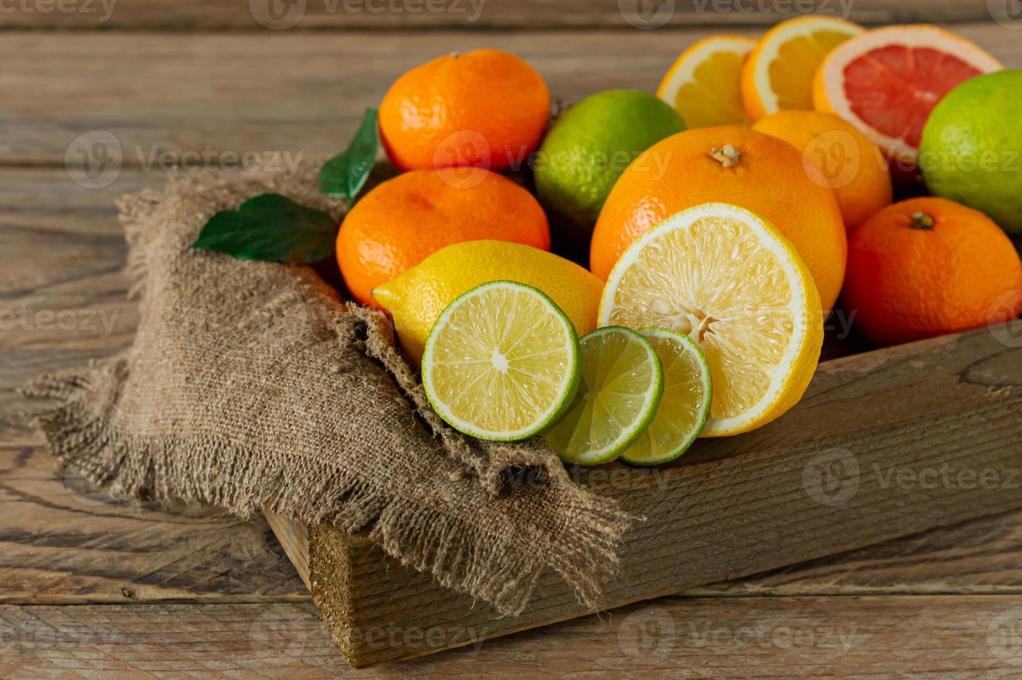 Assorted citrus fruits in a wooden box. Orange, tangerine, grapefruit, lemon and lime. On a wooden background photo