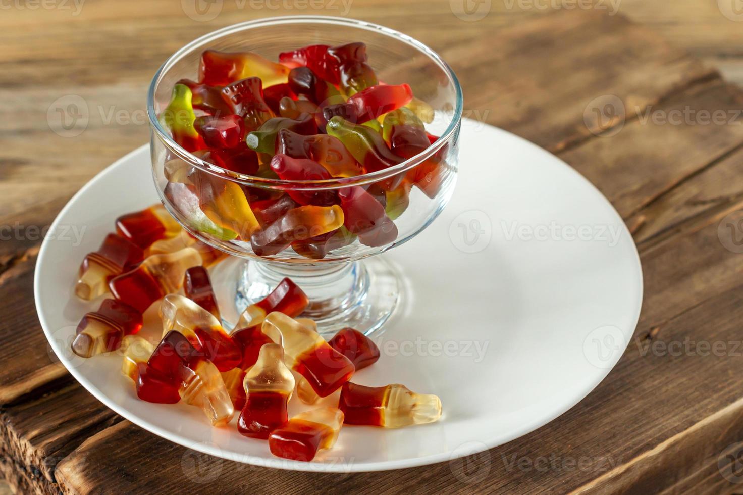 Chewing marmalade bottles of cola and bears on white plate on wooden background. photo