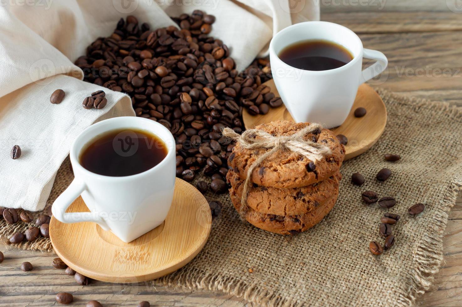 Two cups of freshly brewed espresso on wooden table. coffee beans and crunchie cookies on light wooden table, rustic style, homemade. photo