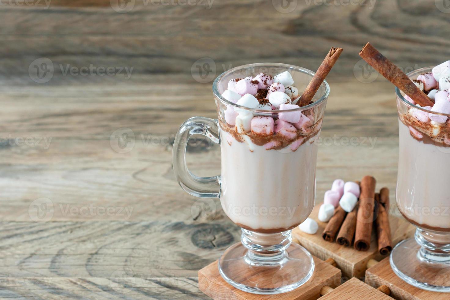 Hot cocoa or chocolate drink with marshmallow in glass mug on wooden table. Concept of cosy Christmas and New Year holidays, copy space photo