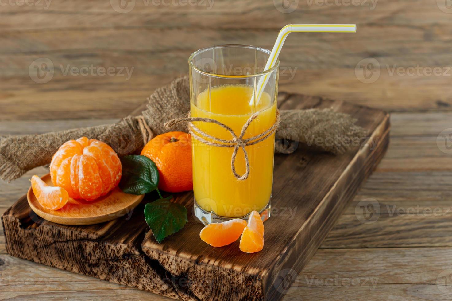 vaso de jugo de mandarina fresca con mandarinas maduras sobre tabla de madera foto