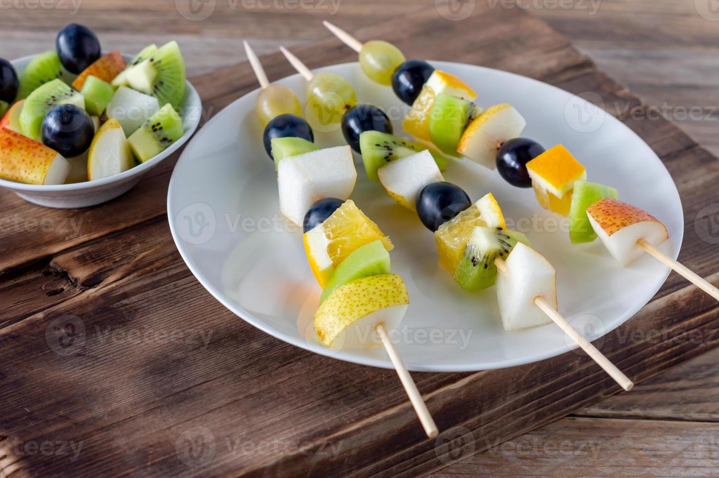 fruit vegetarian canape at skewers with grapes, kiwi and mango at wooden background. catering snack photo