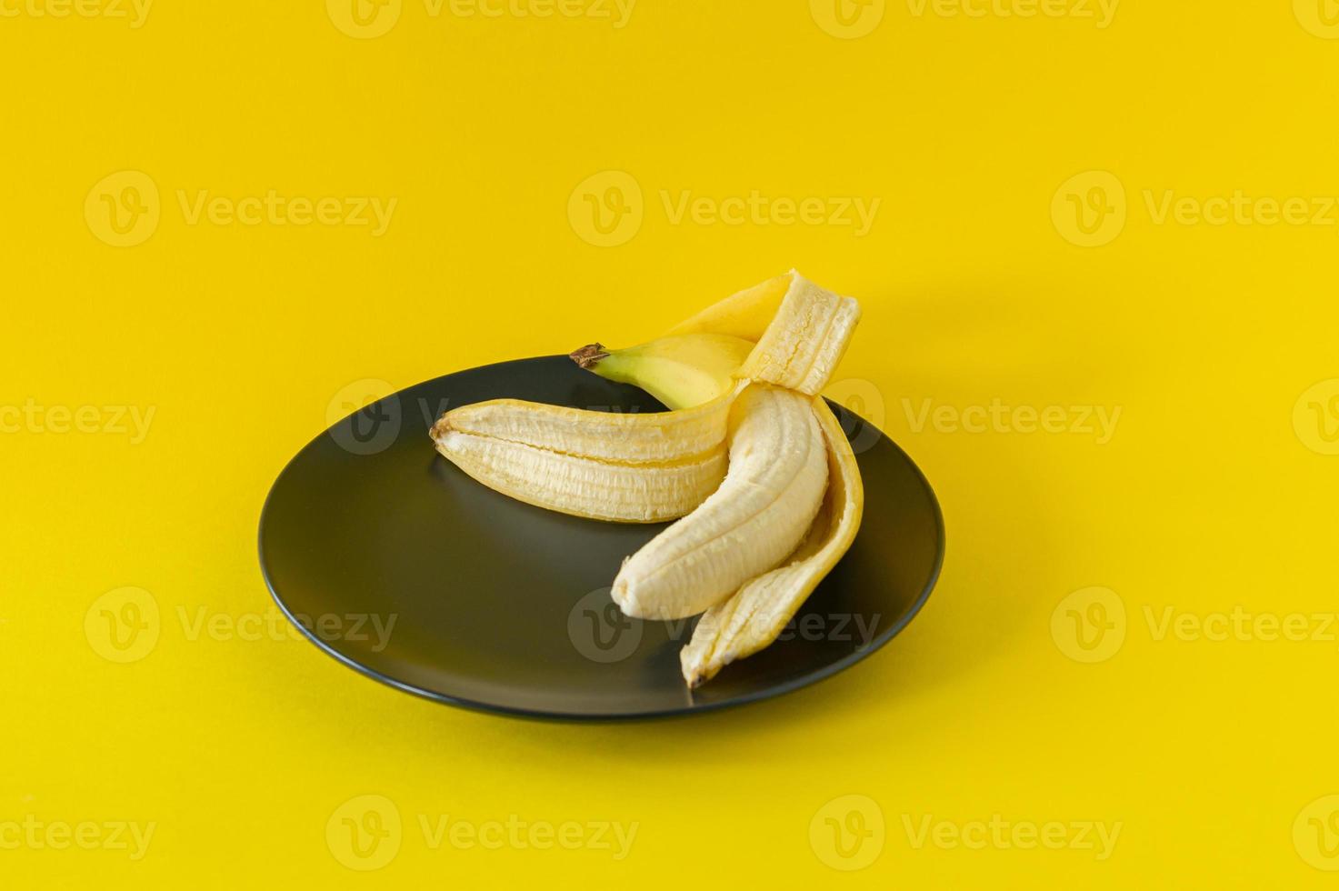 Ripe banana on black plate on yellow background. Tropical fruits for eating photo