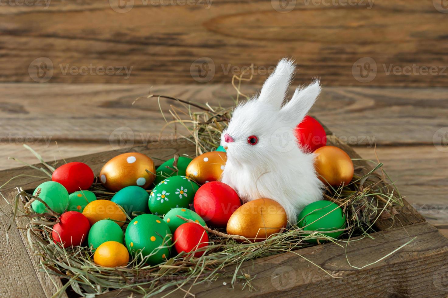 composición festiva de pascua con un pequeño conejito sentado en una caja de madera con huevos de pascua. concepto de estilo rústico, ecológico y granjero foto