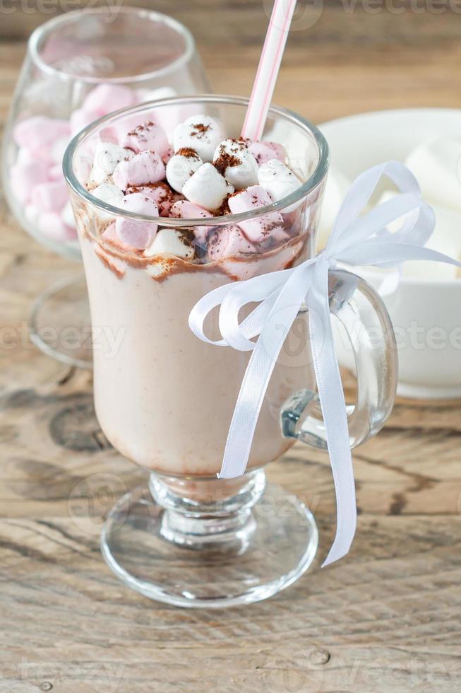 Hot cocoa or chocolate drink with marshmallow in glass mug on wooden table. Concept of cosy Christmas and New Year holidays, copy space photo