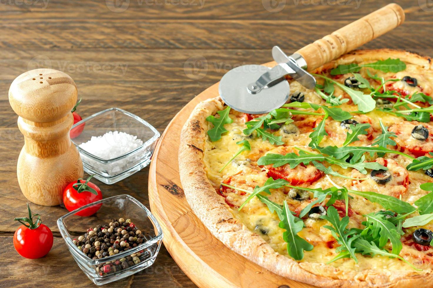pastel de pizza caliente cocinado con pepperoni, tomates, aceitunas negras, rúcula y mozzarella sobre tabla de madera. foto