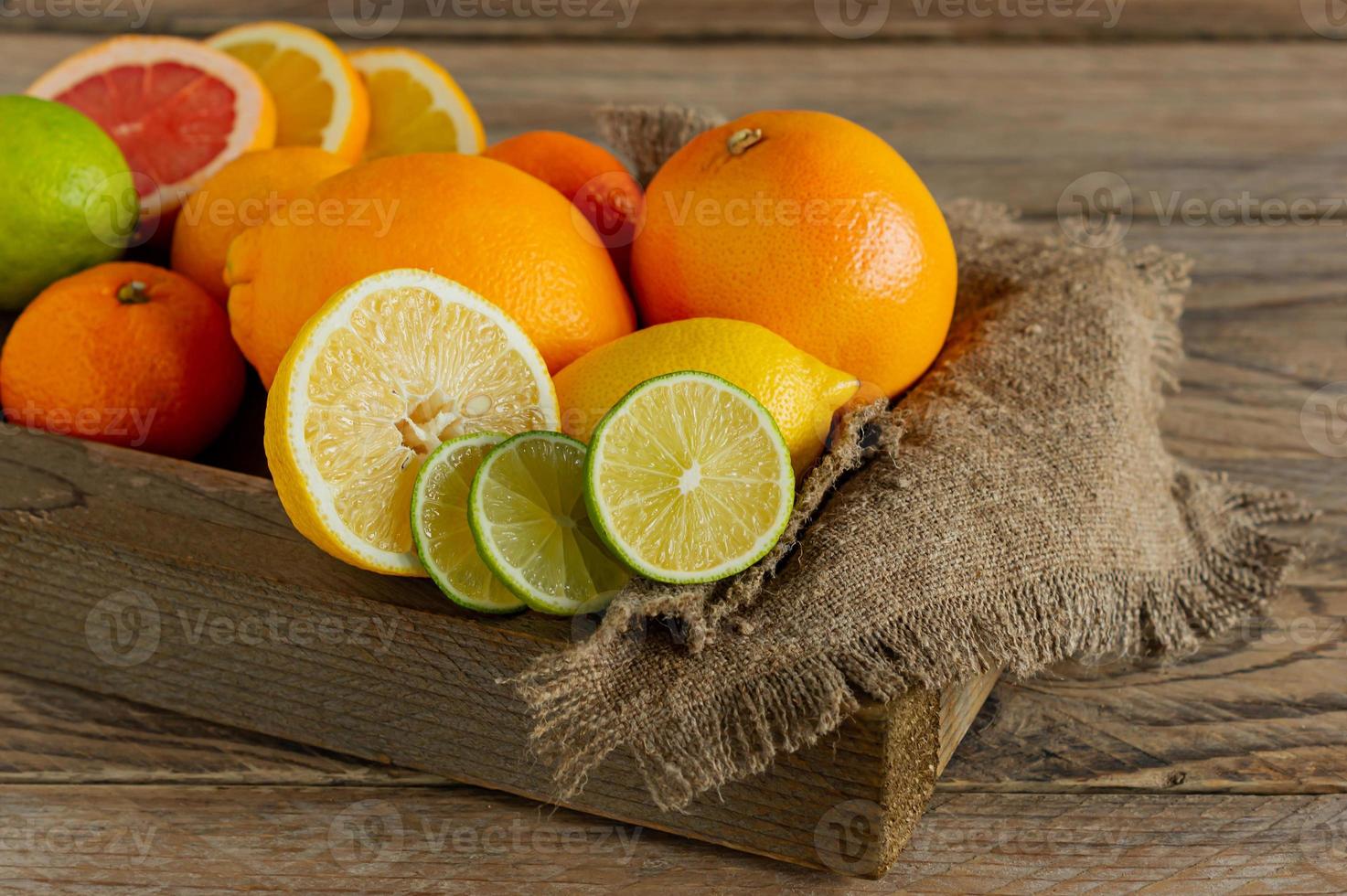 Assorted citrus fruits in a wooden box. Orange, tangerine, grapefruit, lemon and lime. On a wooden background photo