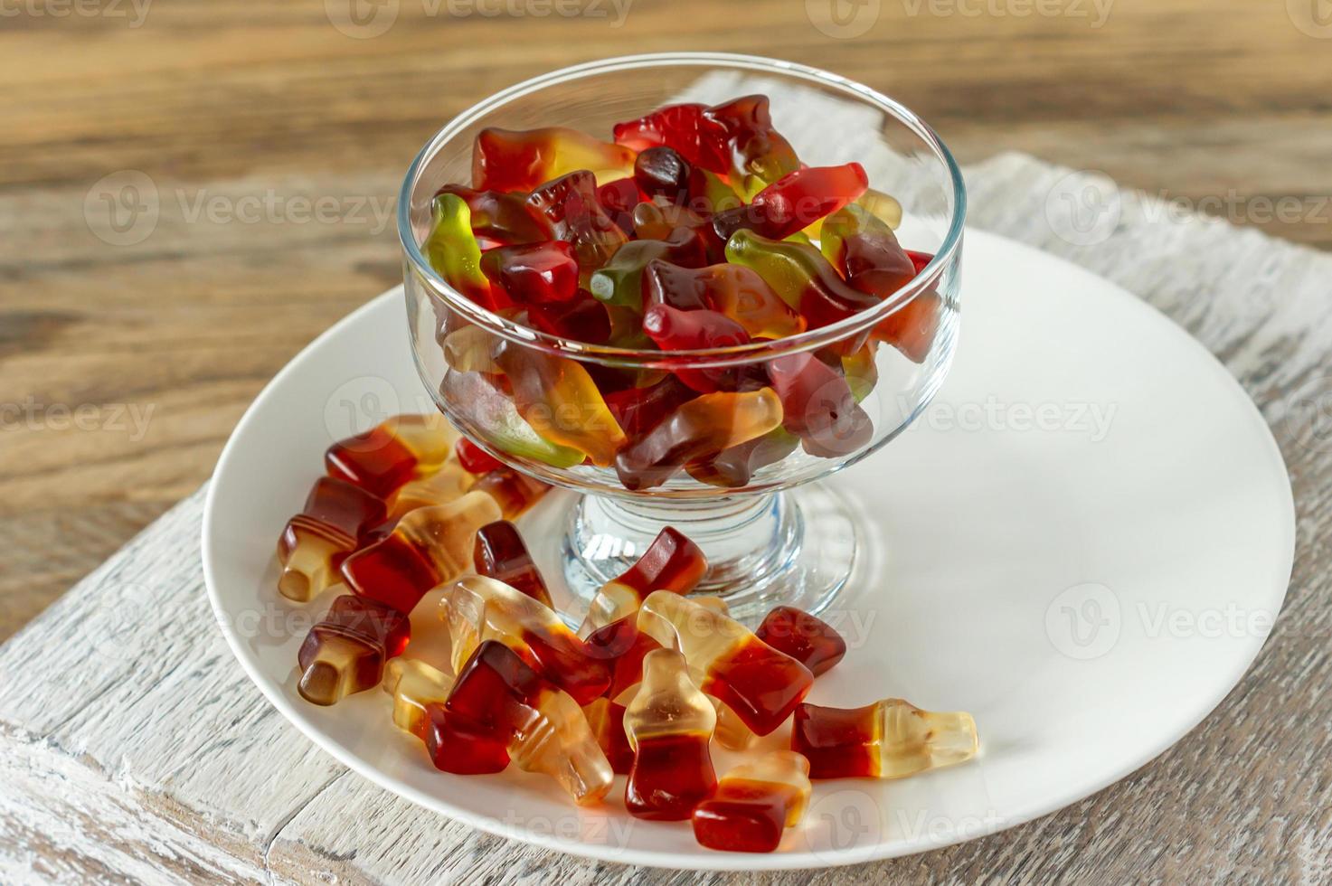 Chewing marmalade bottles of cola and bears on white plate on wooden background. photo