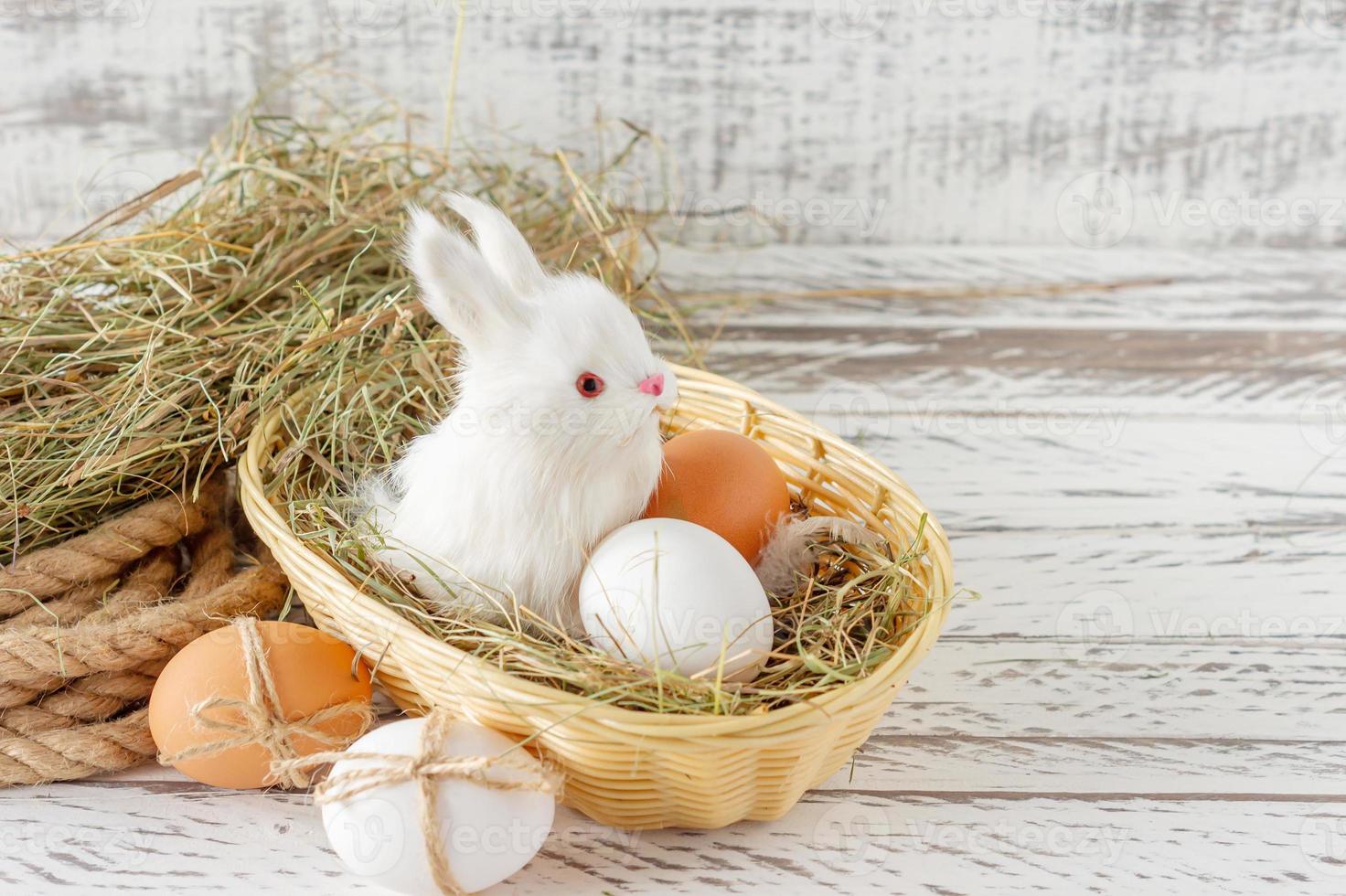 composición festiva de pascua con un pequeño conejito sentado en una canasta con huevo de pascua. concepto de estilo rústico, ecológico y granjero foto