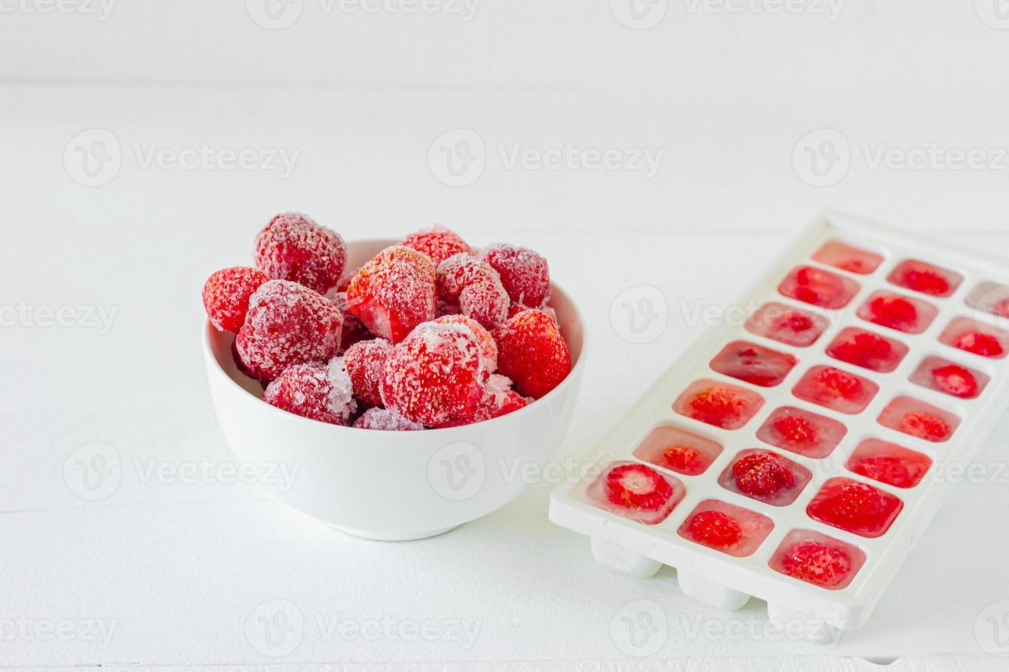 fresas maduras frescas congeladas en cubitos de hielo sobre fondo blanco. alimentación saludable de verano. foto