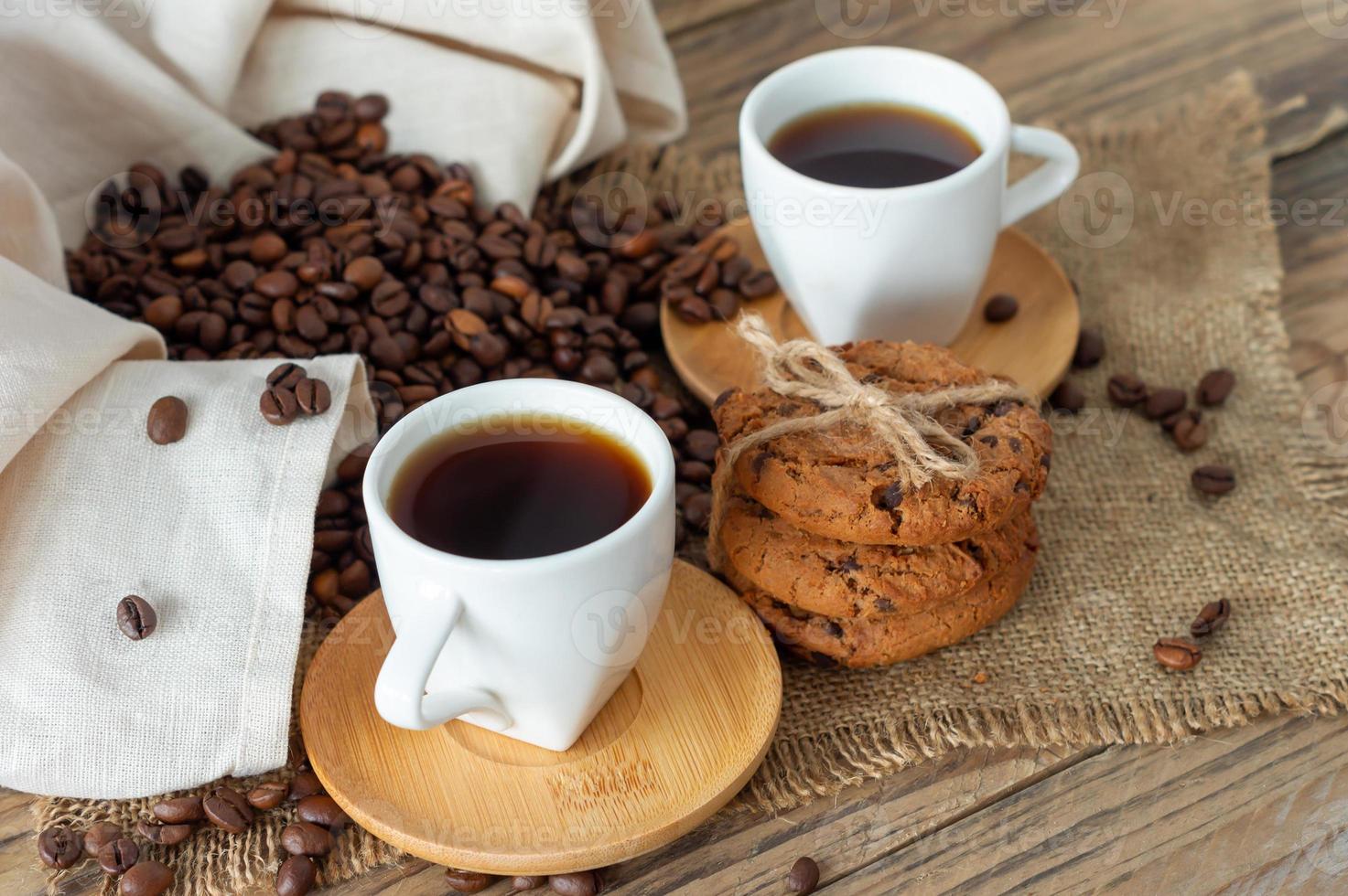 dos tazas de espresso recién hecho en una mesa de madera. granos de café y galletas crujientes sobre una mesa de madera clara, estilo rústico, casero. foto