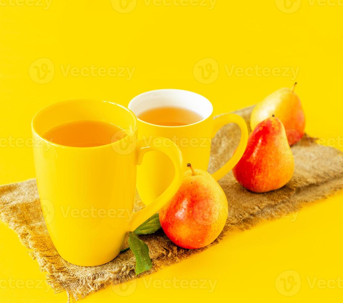 dos tazas de jugo de pera y peras maduras sobre tela de arpillera y fondo amarillo foto