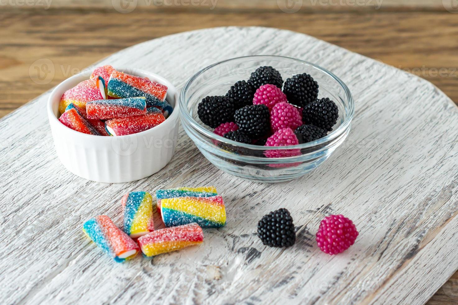 Multi-colored chewing marmalade candies in bowls on wooden cutting board photo