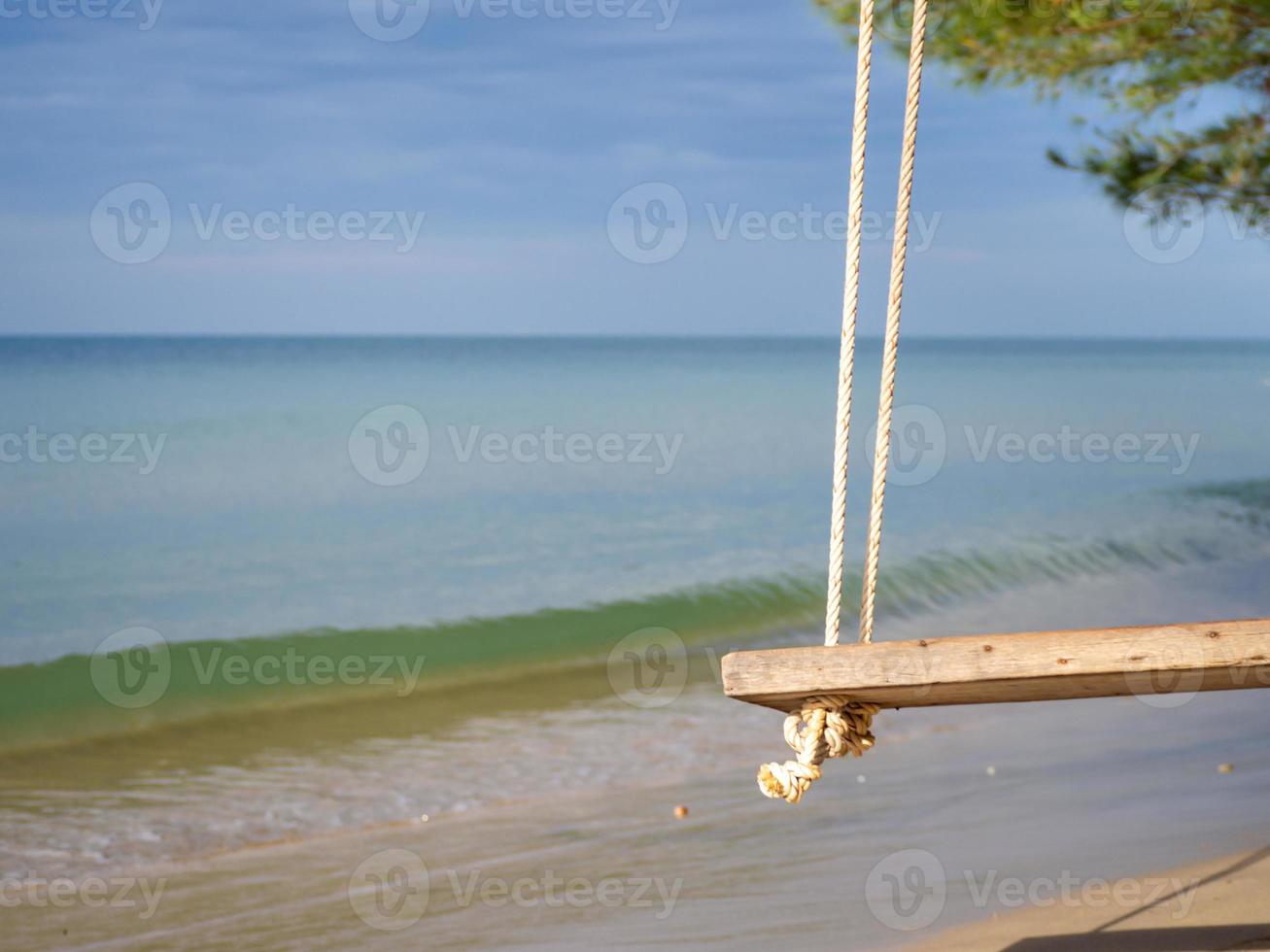 Wooden swing hanging on the tree On the background is a blue sea. photo