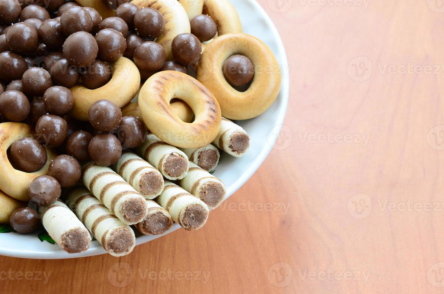 Crispy tubules, chocolate melting balls and bagels lie in a white plate on a wooden table. Mix of various sweets photo
