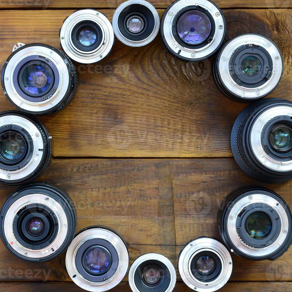 Several photographic lenses lie on a brown wooden background. Space for text photo