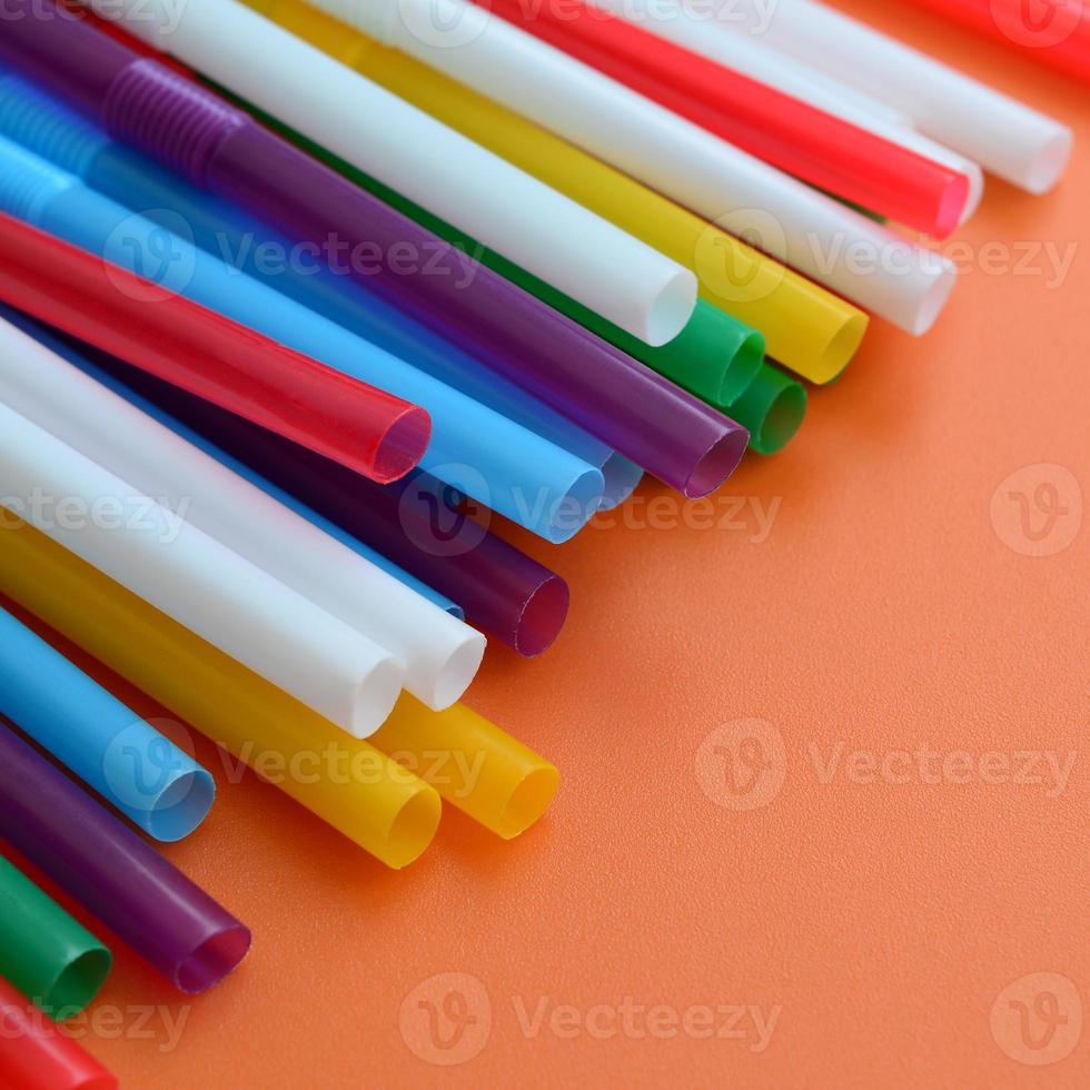 Many colorful straws for drinks lies on a bright orange background surface photo