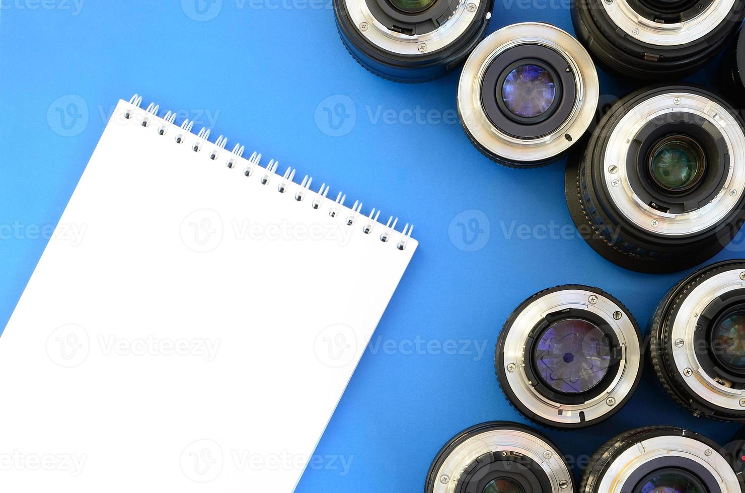 Several photographic lenses and white notebook lie on a bright blue background. Space for text photo
