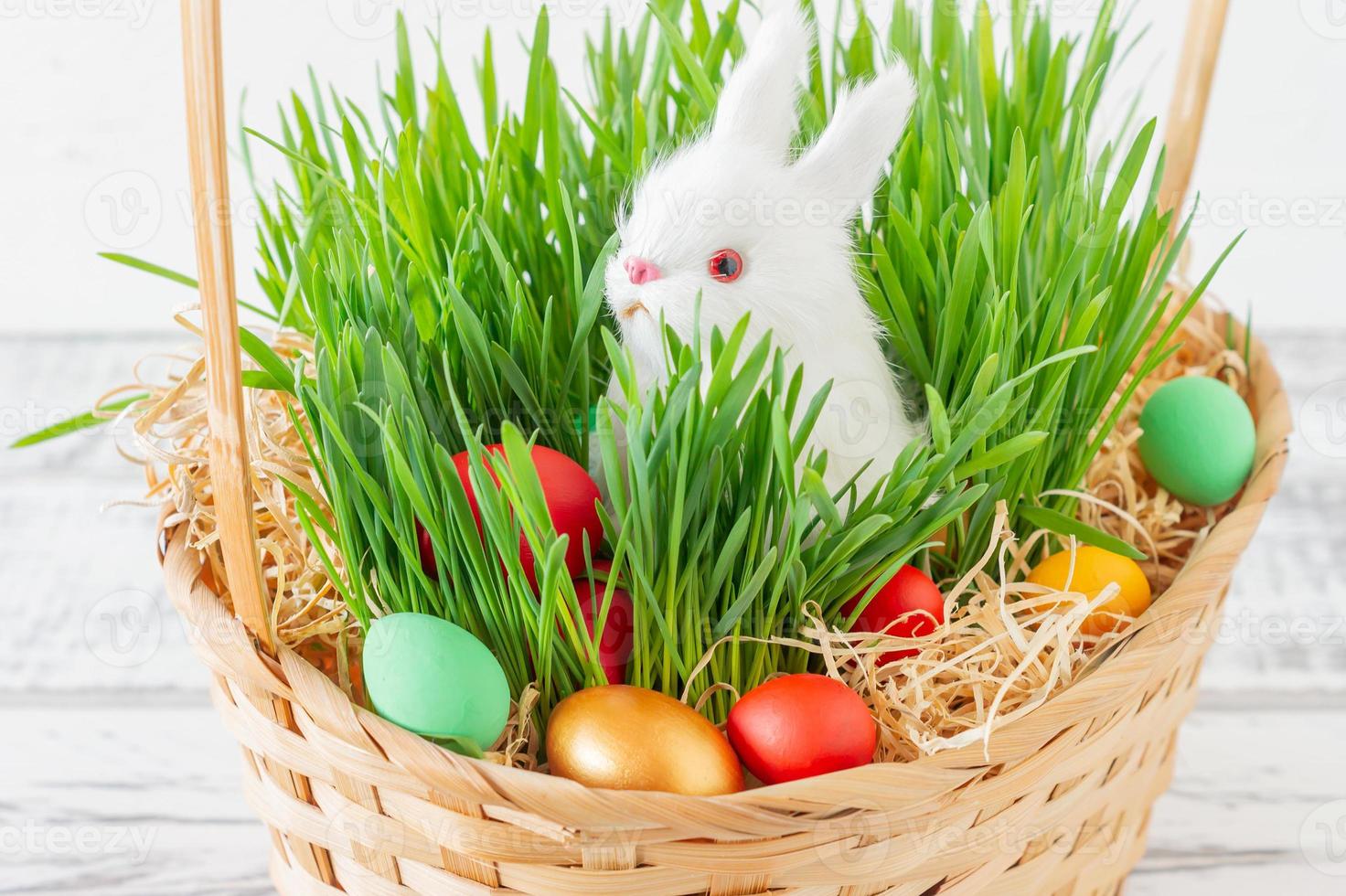 Easter basket with green grass filled with brightly colored Easter eggs and White little bunny. Happy Easter. photo